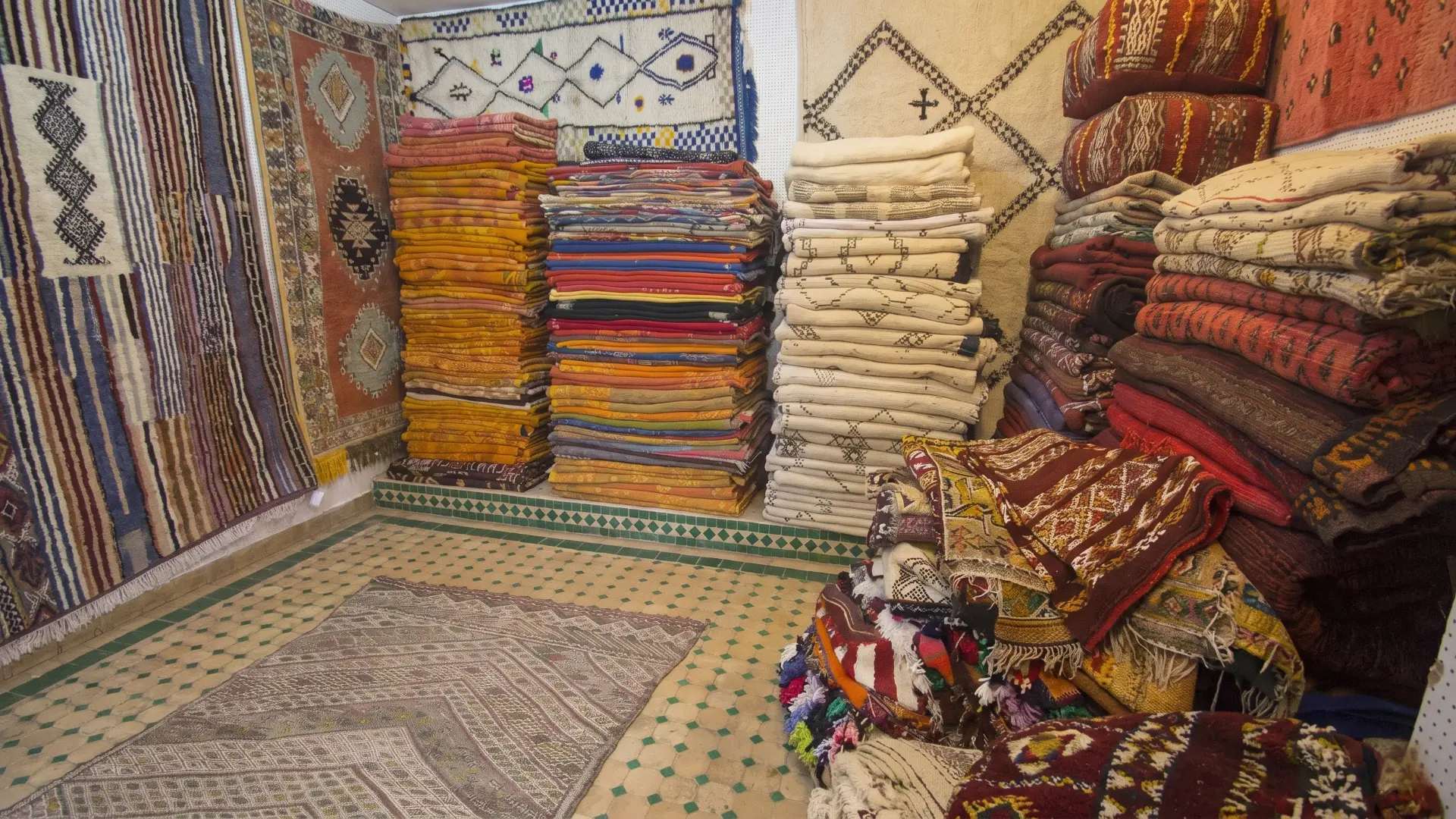 Traditional Carpet Shop Fez Medina | Colorful Moroccan Rugs & Textiles Stacks of vibrant handmade Berber rugs and textiles in a traditional shop in the Fez Medina Morocco